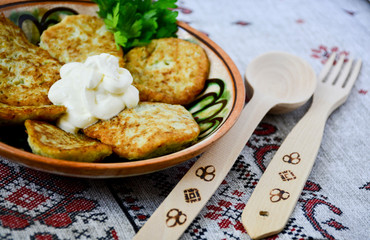 Traditional Slavic cuisine potato pancakes. Potato pancakes. Food served on a clay plate with sour cream. In ancient times, a wooden spoon and a wooden fork were sold. The towel is decorated with a n