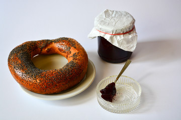 Fresh donated crispy bagel with poppy seeds on a white plate with tasty natural apricot jam and a...