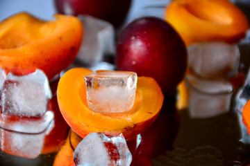 Apricots and plums fruits lie on a mirror surface with ice cubes. The water from the melting ice and the fruits reflected in the mirror create a wonderful composition. White ice contrasts with fruits.
