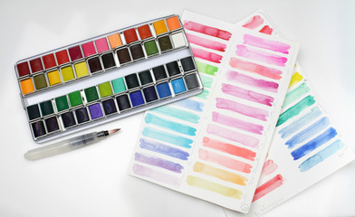 Box with watercolors, brush and palette on a light gray paper background.