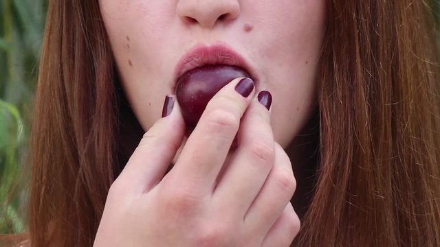  A girl near school eats a plum and licks her sweet lips.