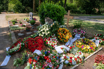 Viele Kränze mit Schleifen unter einem Holzkreuz