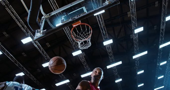 Low angle of professional basketball player in action performing slam dunk in a basketball hoop on a sports arena
