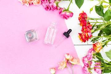 Skin Care Cosmetics in a Frame of Fresh Roses. Essence, Oil on a pink and white desk.