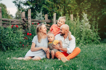 Fototapeta premium Beautiful happy Caucasian Ukrainian family of four people in park on summer day. Mother and father hugging their two sons brothers siblings. Lifestyle authentic natural emotions moment.