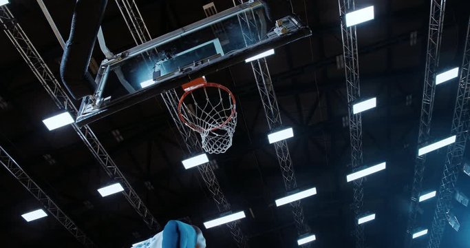 Low angle of professional basketball player in action performing slam dunk in a basketball hoop on a sports arena