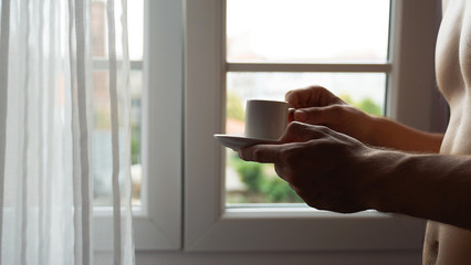 man hands holding small cup of coffee near window in morning sunlight