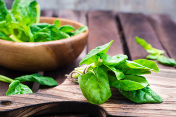 A bunch of fresh baby spinach leaves on a cutting board and spinach leaves in a bowl on a wooden table