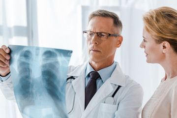happy woman looking at doctor in white coat holding x-ray in clinic