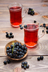 Bowl with black currant berries and fresh compote of ripe black currant in a glass on a wooden table