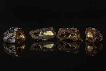 Group of four halves of dried brown date medjool isolated on black glass