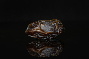 One whole dried brown date medjool isolated on black glass