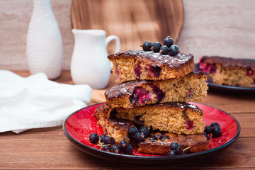 Slices of sweet cake with black currant on a plate on a wooden table