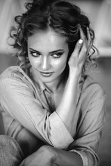 Pretty cheerful blonde young woman with curly hair and charming smile resting in her home, room with modern scandinavian interior
