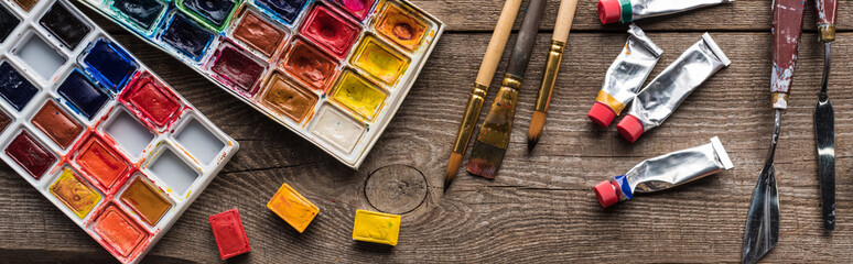 top view of colorful paint palettes and drawing tools on wooden surface, panoramic shot