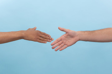 Closeup shot of human holding hands isolated on blue studio background. Concept of human relations, friendship, partnership, business or family. Copyspace.