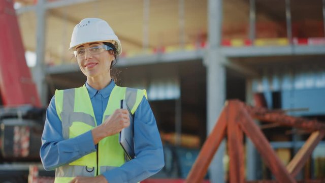 Portrait of Beautiful Female Architectural Engineer / Safety Inspector / Investor closes Laptop, Crosses Arms on the Commercial Building Construction Site. In the Background Skyscraper Formwork Frames