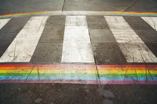 Road marking of pedestrian crossing and rainbow flag in Paris. Sex discrimination concept. Selective focus. The symbol of the LGBT community, equal rights