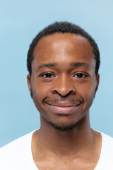 Obraz premium Close up portrait of young african-american man in white shirt on blue background. Human emotions, facial expression, ad, sales concept. Looks calm. Looking at camera.