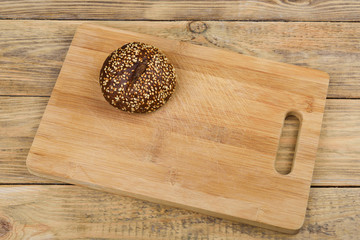 Malt bread with sesame seeds on a cutting board over a wooden table.
