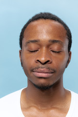 Obraz premium Close up portrait of young african-american man in white shirt on blue background. Human emotions, facial expression, ad, sales concept. Looks calm. Standing with eyes closed and dreaming.