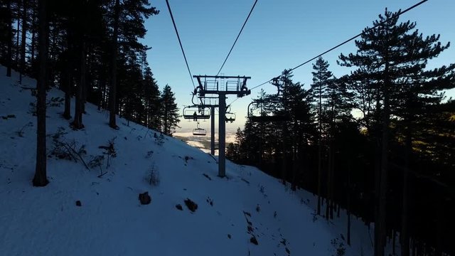 POV travelling on ski resort cable lift in shaded snow covered mountain slope.