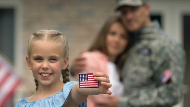 Smiling girl showing american flag patch, hugging parents on background, patriot