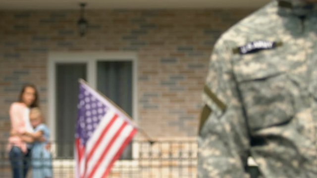 Sad serviceman leaving house looking wife and daughter hugging background, duty