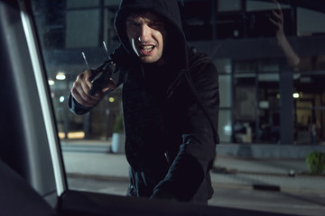 aggressive thief in black hoodie pointing gun at car window
