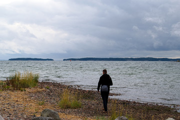 A man walks on a pebble beach with a bag  