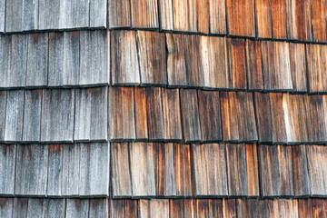 Weathered and faded from the sun wooden shingles that are the facade of an alpine house. Wooden...