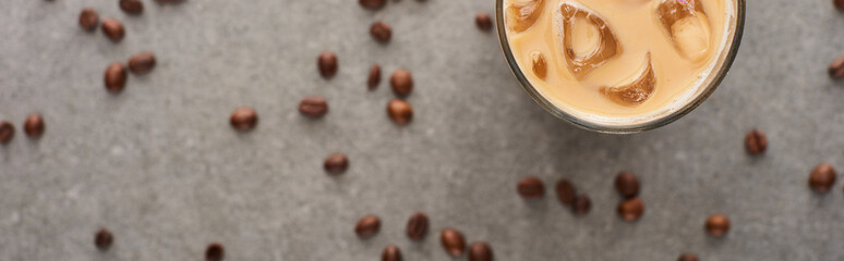 selective focus of ice coffee in glass and coffee grains on grey background, panoramic shot