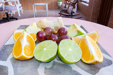 Orange, banana, lemon, apple and grapes, slices on top of a plate