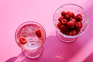 Sparkling water with raspberries in a Champagne glass, isolated on pink gradient background.