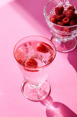 Sparkling water with raspberries in a Champagne glass, isolated on pink gradient background.
