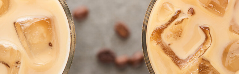 close up view of ice coffee in glasses and coffee grains on grey background, panoramic shot