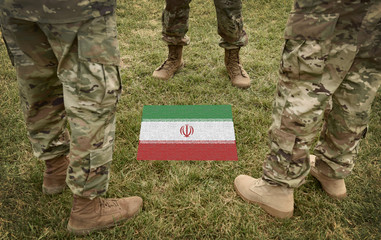 Flag of Iran and US soldiers legs on the grass (collage).