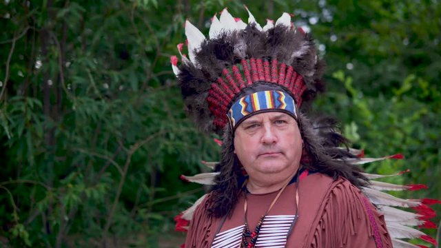 Old Native American Indians stands against the background of the forest with a serious face