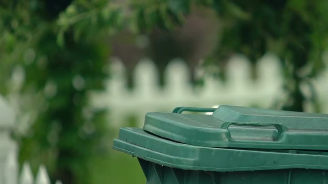 Man throwing garbage bag in green plastic container, waste utilization, ecology