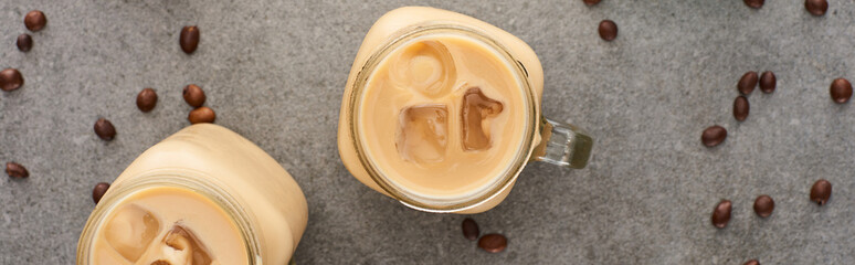 top view of ice coffee in glass jars and coffee grains on grey background, panoramic shot