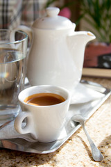 Close-up on a tray white porcelain coffee pot and a cup with freshly brewed espresso on the terrace, selective focus