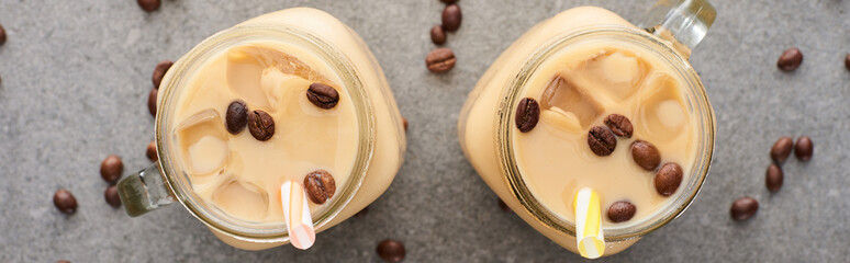 top view of ice coffee in glass jars with straws and coffee grains on grey background, panoramic shot