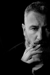 Black and white portrait of a brutal gray haired man with a beard with a yellow flower in his hands on a black background, selective focus