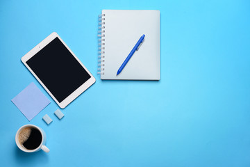 Modern tablet computer with cup of coffee and stationery on color background