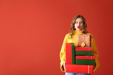 Confused young woman with Christmas gifts on color background