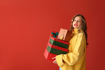 Confused young woman with Christmas gifts on color background