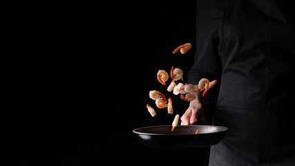 Seafood, chef prepares shrimps in a frying pan, roasts. On a black background for design, menus, restaurants, oriental cuisine, healthy food. Horizontal photo, banner