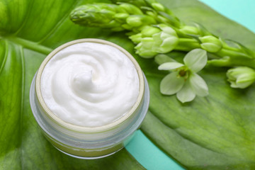 Obraz na płótnie Canvas Jar of natural cream, green leaf and flowers on color background