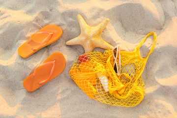 Flip-flops with mesh bag, sunglasses and cosmetics on sand beach