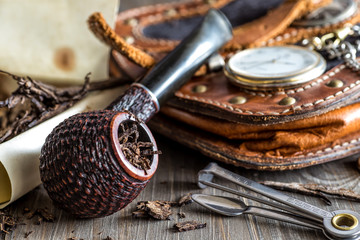Wooden pipe with tobacco on wooden table. Tin boxes with tobacco, pipes and vintage background....